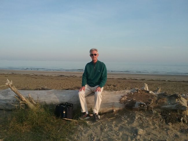 gentleman sitting on a piece of driftwood on the beach