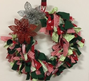 Christmas wreath made from strips of material , accented by two glittery poinsettias