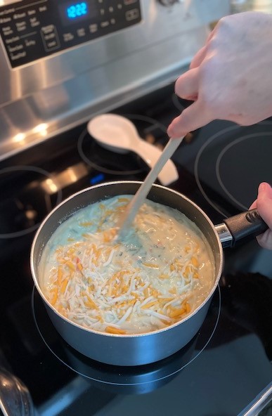 shredded cheese being stirred into the broccoli soup base