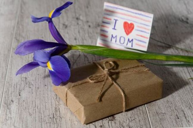 brown package tied with twine and a blue iris flower next to a notecard that reads I heart Mom