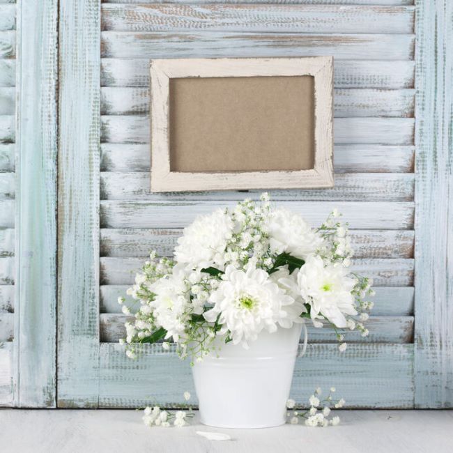 Worn shutter with a bouquet of white cushion daisies in a white tin bucket
