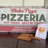 Pizza themed sign with a pizza cutter and a decorative towel