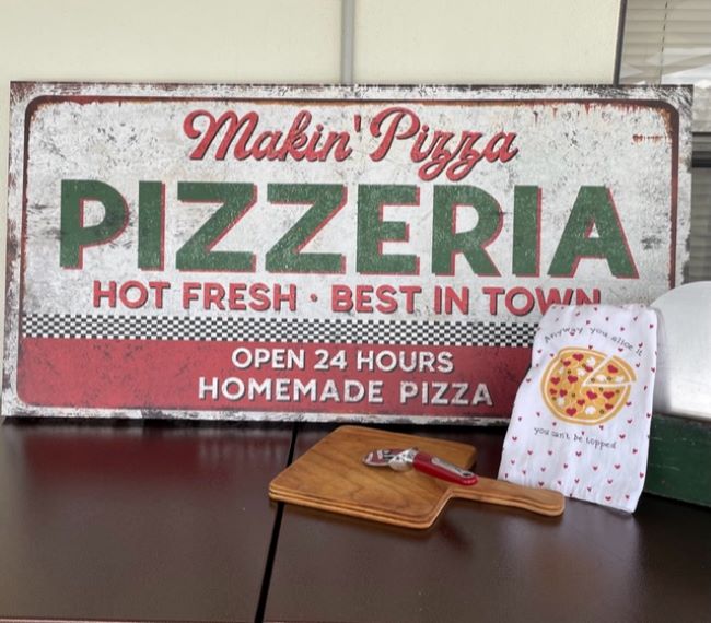 Pizza themed sign with a pizza cutter and a decorative towel