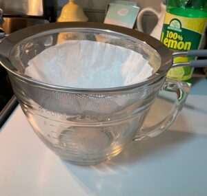 mesh strainer lined with a coffee filter placed on top of a large glass measuring cup