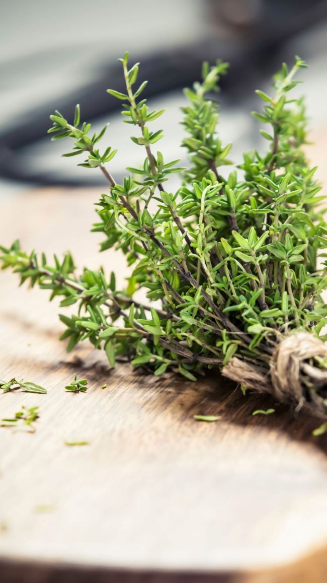 fresh thyme gathered into a bundle, displayed on a wooden cutting board