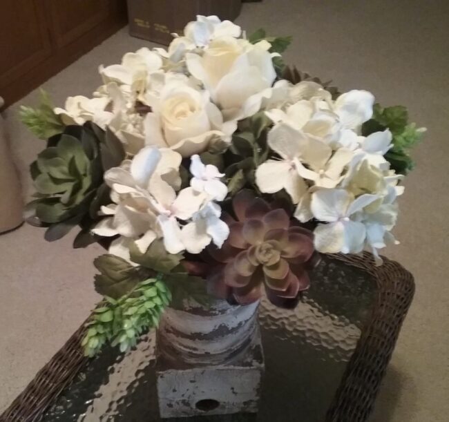 Assorted creamy white silk flowers accented with faux succulents in a round bowl
