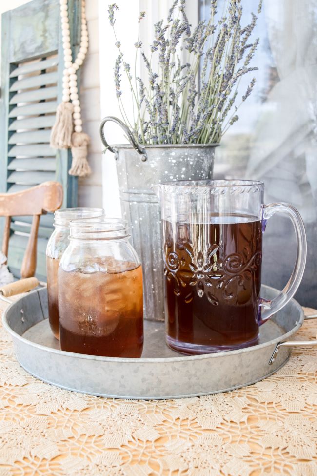 close up view of galvanized tray holding a pitcher of iced tea and two mason jars of tea accented with a bucket of french lavender