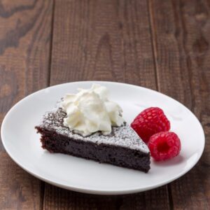 piece of chocolate sponge type cake with powdered sugar and whipped topping on a white plate