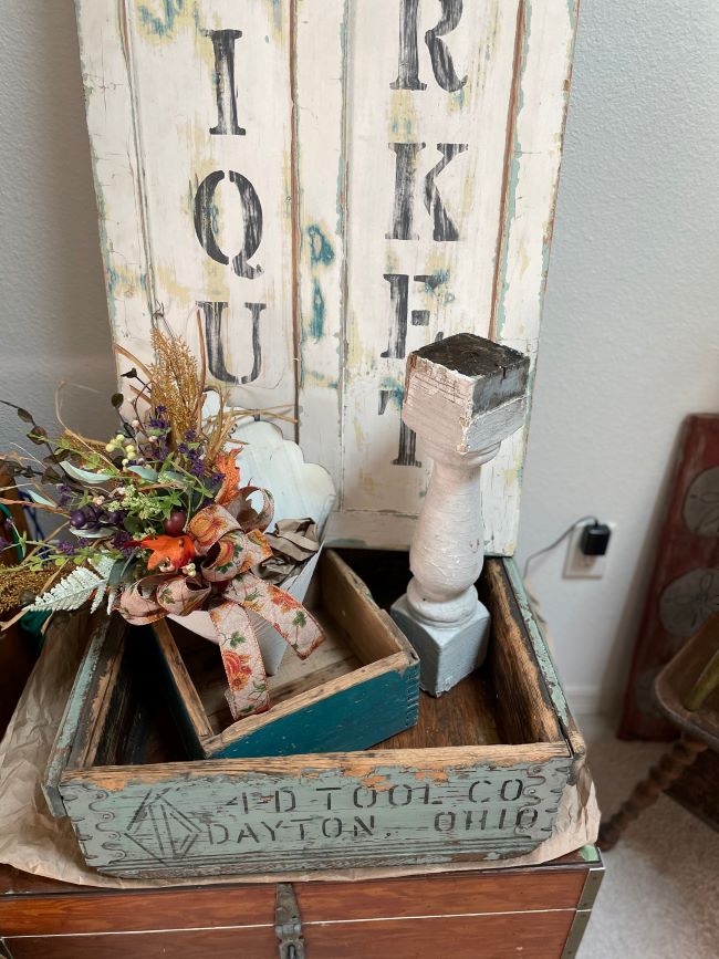 wooden boxes stacked on top of old sea chest. Autumn arrangement in a wall pocket made of barn tin. Decorative sign made from old door