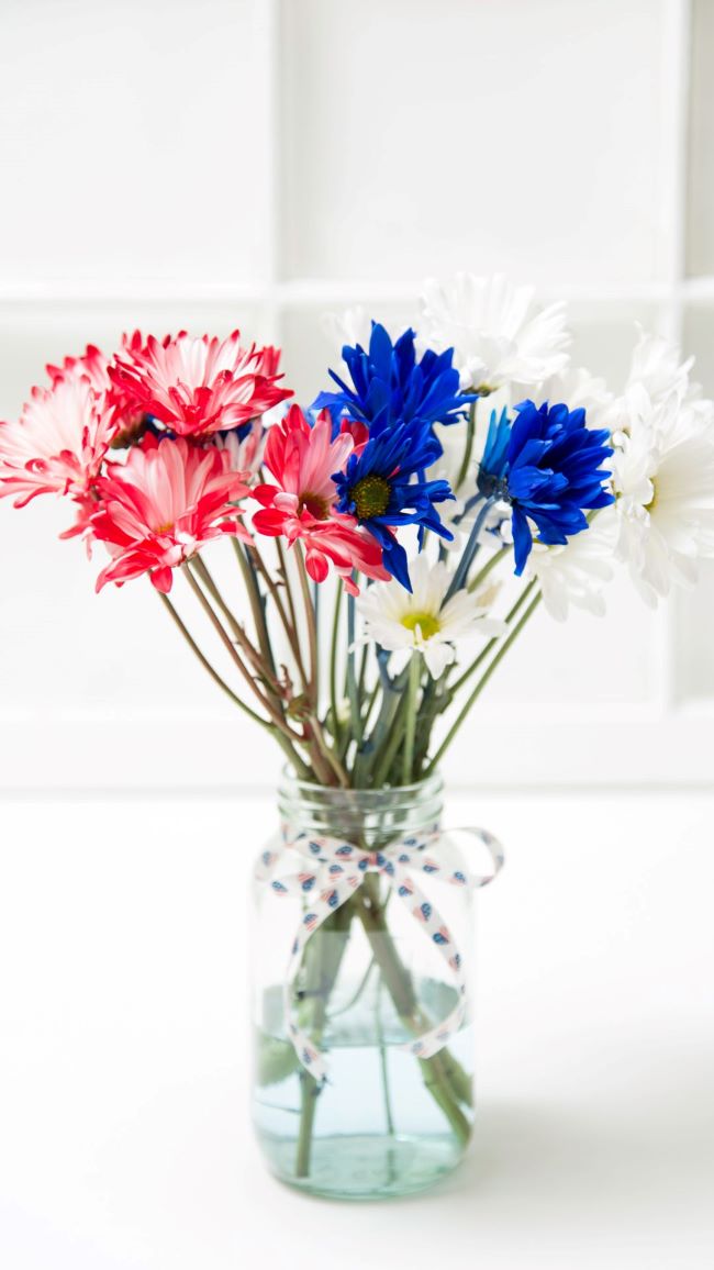 red white & blue daisies in a clear mason jar with shoestring bow