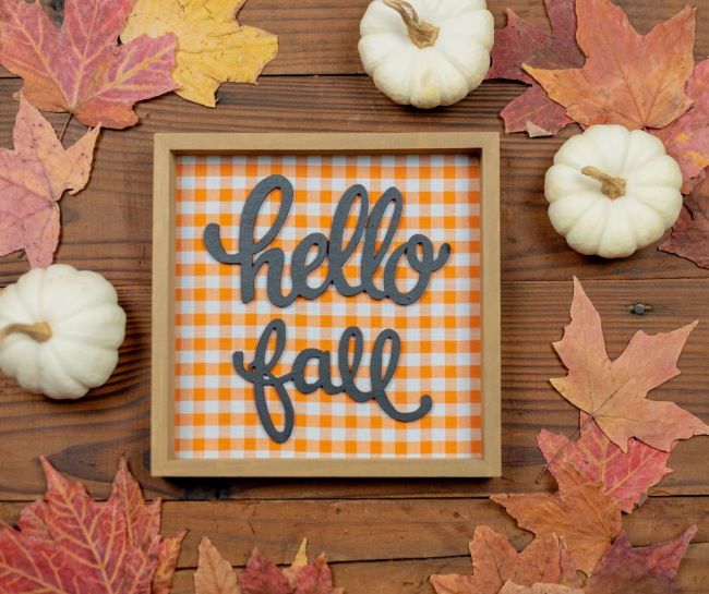 "hello Fall" sign on a table surrounded by white pumpkins and leaves