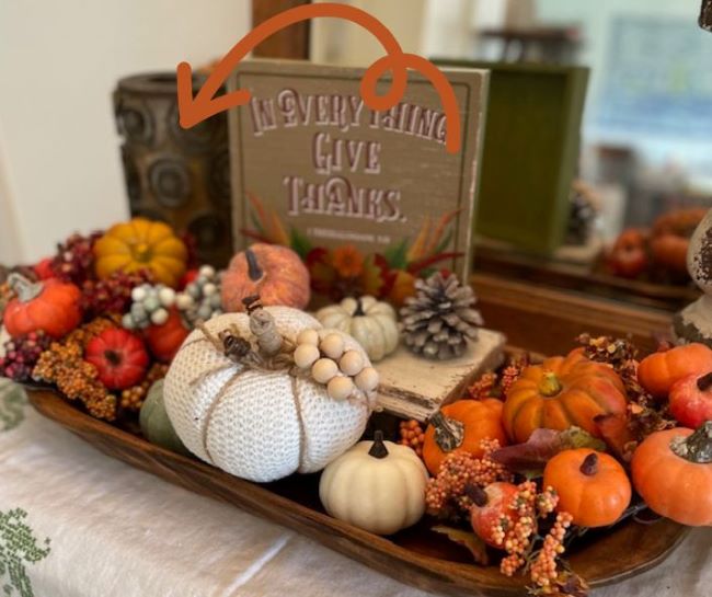 wooden dough bowl with faux pumpkins with an arrow pointing to an antique wallpaper roller