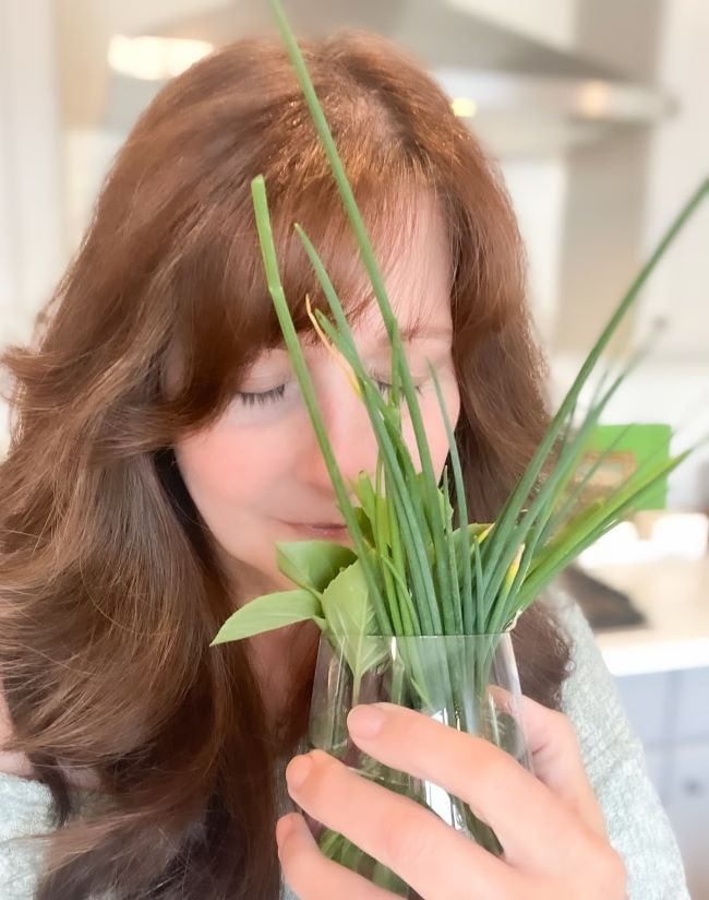 woman enjoying the fragrance of a vase filled with fresh cut herbs