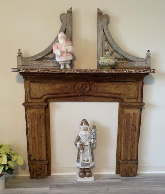 rustic fireplace mantel decorated with a pink Santa and two corbels