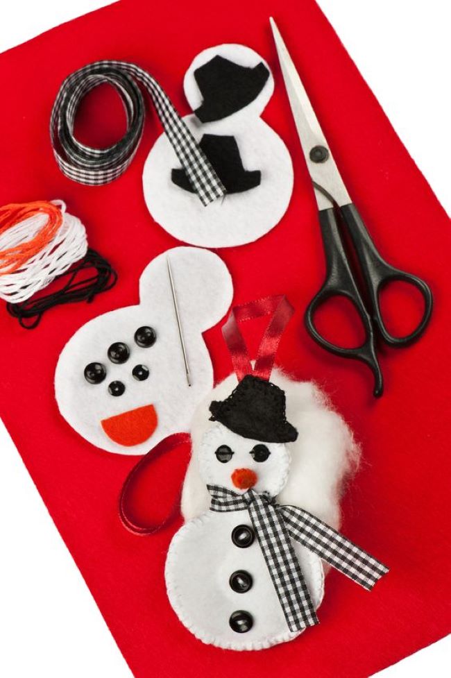 piece of red felt with white felt snowmen, thread, ribbon and scissors