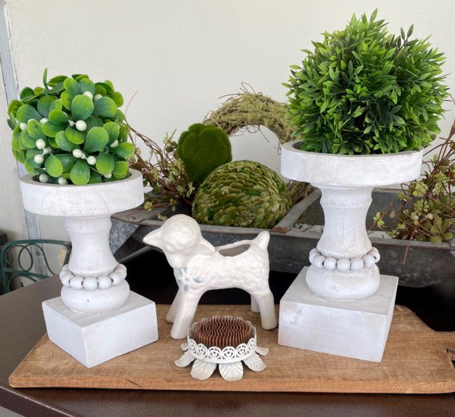 vintage ceramic lamb, old metal flower frog, wooden candle holders in front of a galvanized hog feeder