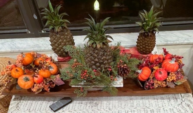 artificial pineapple, pinecones and pumpkins arranged in a long dough bowl