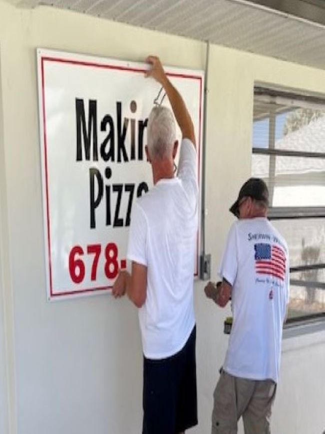 two men hanging metal sign on wall