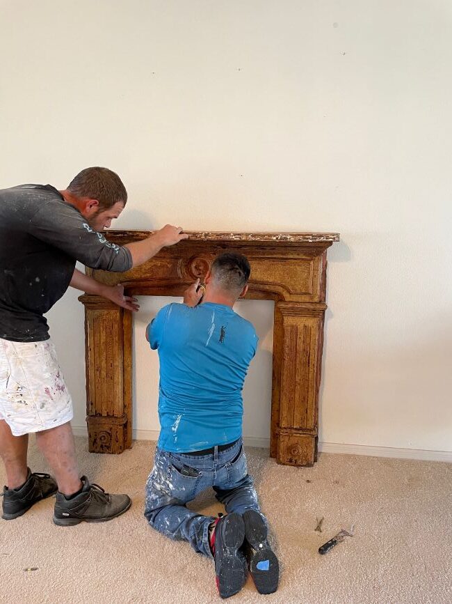 two guys attaching reclaimed fireplace mantel to the wall