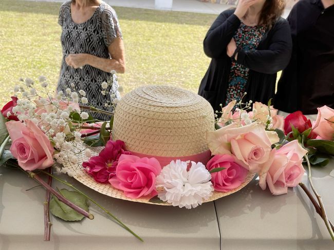 straw hat decorated with artificial flowers, surrounded by fresh roses