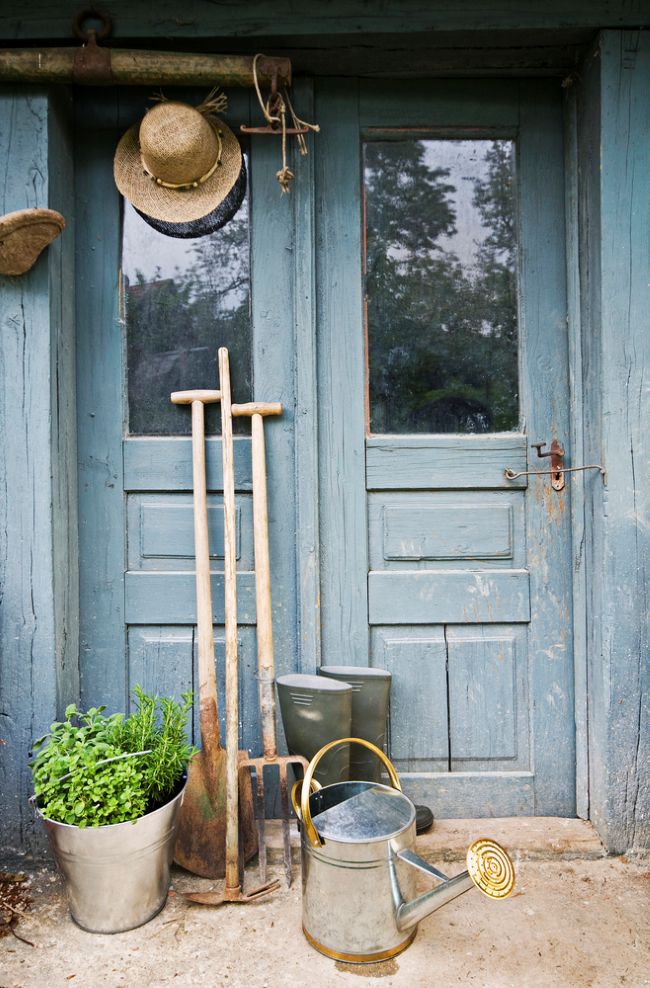 old blue door with pail of herbs, watering can, rubber boot and garden tools
