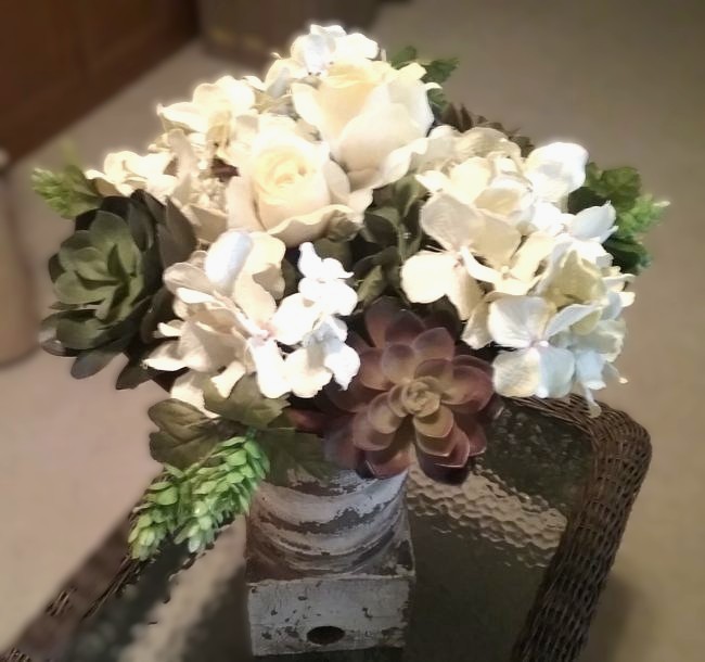 Soft white hydrangeas and greenery arranged in a rustic vase on a wicker table, styled in a calm cream and green spring palette