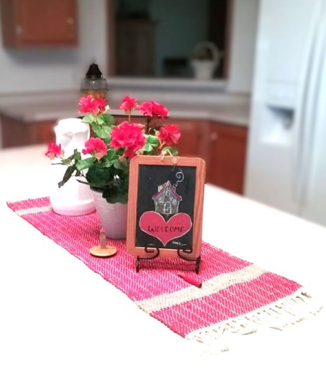 vignette on kitchen island with red flowers, white carafe, chalkboard