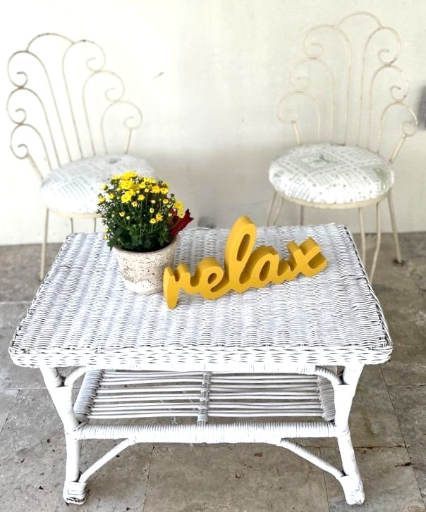 vintage white wicker coffee table with two ice cream chairs and a wood Relax sign