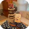 Patriotic 4th of July vignette with an Uncle Sam hat holding small American flags, a vintage postcard, and a rustic pedestal on blue floral fabric