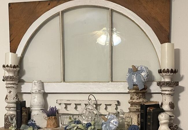 old window hung over a fireplace mantel. Mantel decorated with architectural salvage pieces