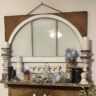 old window hung over a fireplace mantel. Mantel decorated with architectural salvage pieces