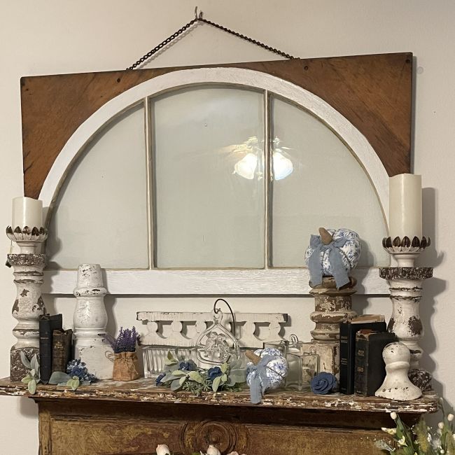 old window hung over a fireplace mantel. Mantel decorated with architectural salvage pieces