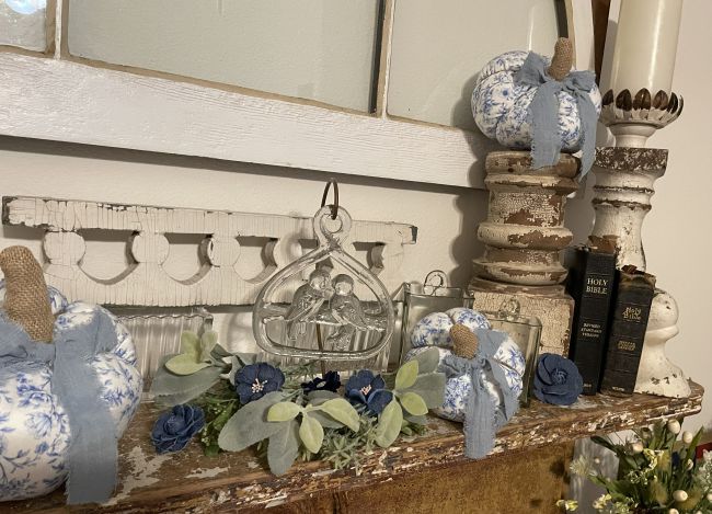 close up photo of a fireplace mantel decorated with an assortment of architectural salvage pieces, old Bibles and blue & white fall decor