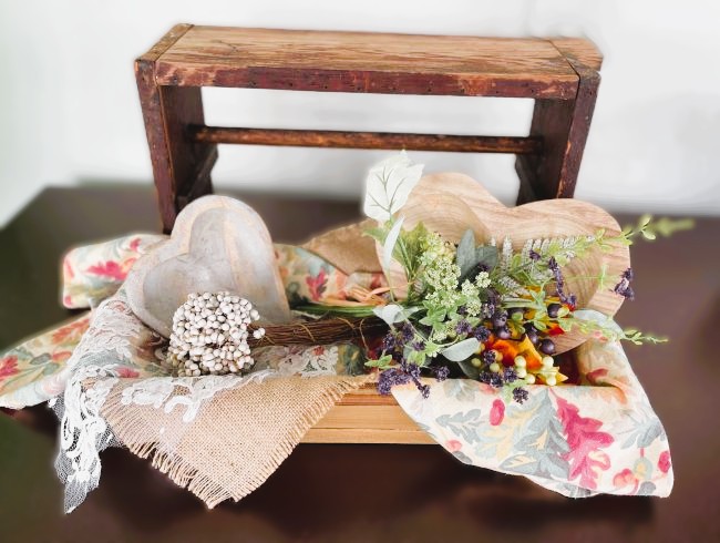 wooden bowl layered with vintage fabric, lace and burlap. Accented with two wooden heart shaped bowls, tallow berries and fall tussies