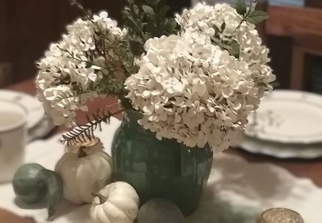 close up of vintage pottery pitcher filled with faux hydrangea and artificial greenery