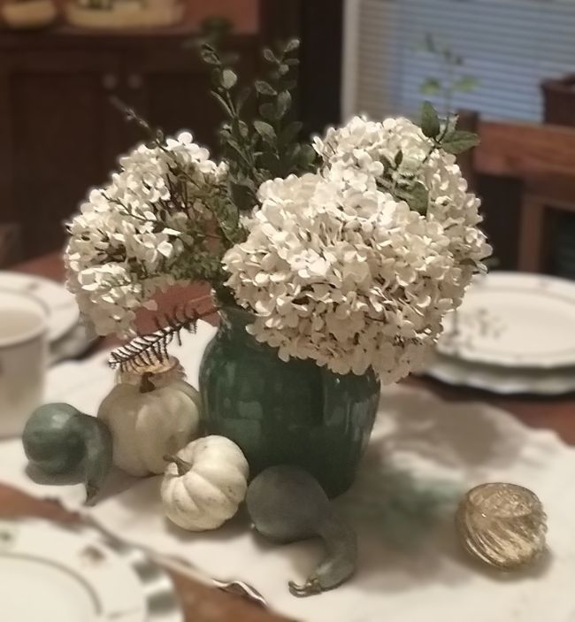 close up of vintage pottery pitcher filled with faux hydrangea and artificial greenery